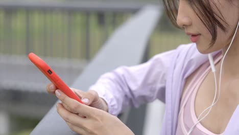 mujer joven asiática de 4k escuchando música desde auriculares y teléfono inteligente mientras corre en el parque público de la ciudad por la mañana.