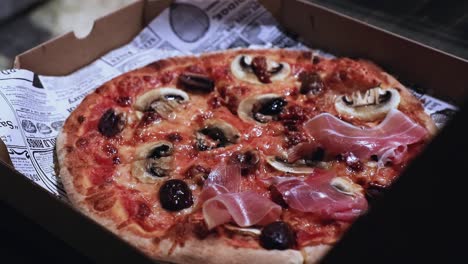 Nahaufnahme-Einer-Köstlichen-Pizza-Im-Karton,-Während-Der-Koch-Prosciutto-Als-Belag-Hinzufügt