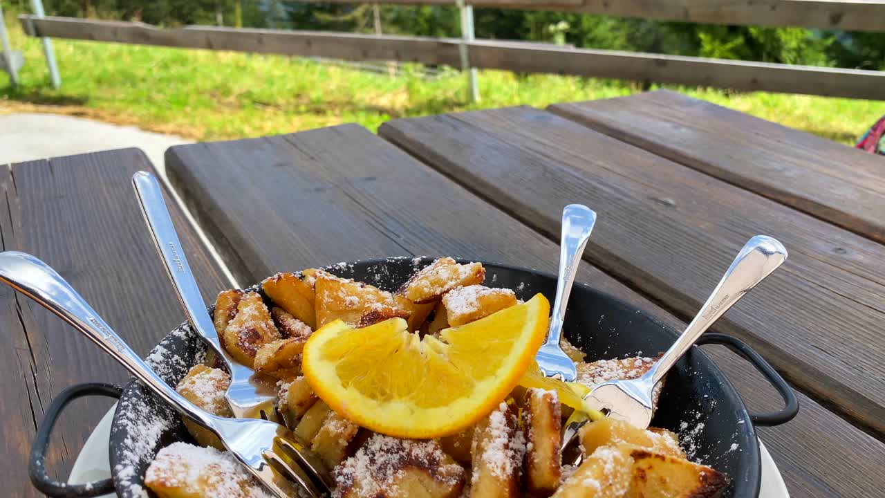 postre tradicional austriaco kaiserschmarren con una impresionante vista de las montañas en tirol austria, dulce panqueque peludo triturado con una naranja en serfaus fiss ladis, verano, tiro de 4k