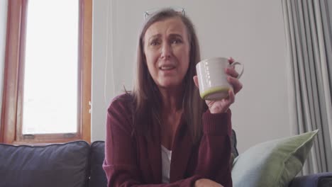 mujer con taza de café hablando en la cámara en casa