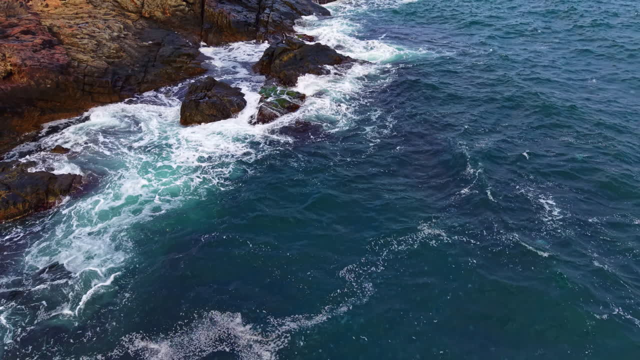Au coucher du soleil, les vagues se brisent contre les rochers escarpés le long d’une côte sereine, créant un magnifique spectacle naturel de la mer et de la pierre.