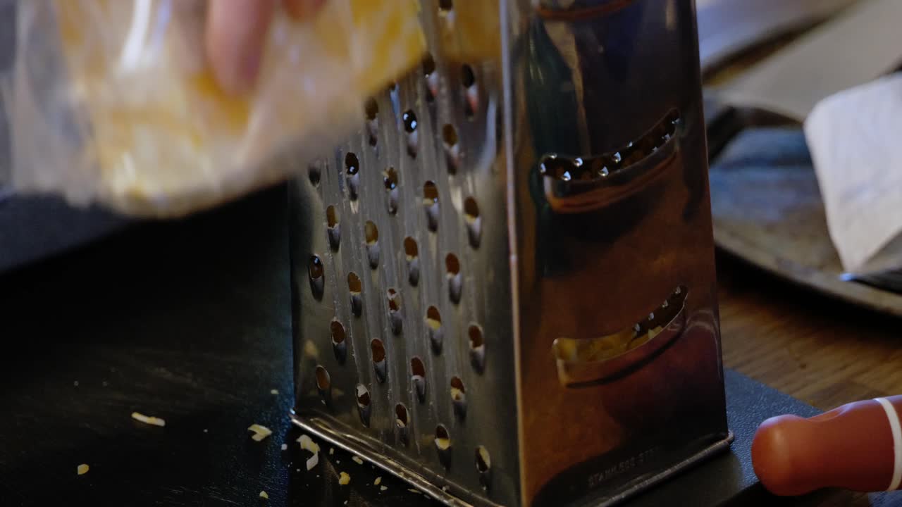 Blocco di formaggio Colby Jack Cheddar grattugiato da una mano bianca caucasica su una grattugia per formaggio in acciaio metallo alluminio - in Cinema 4k