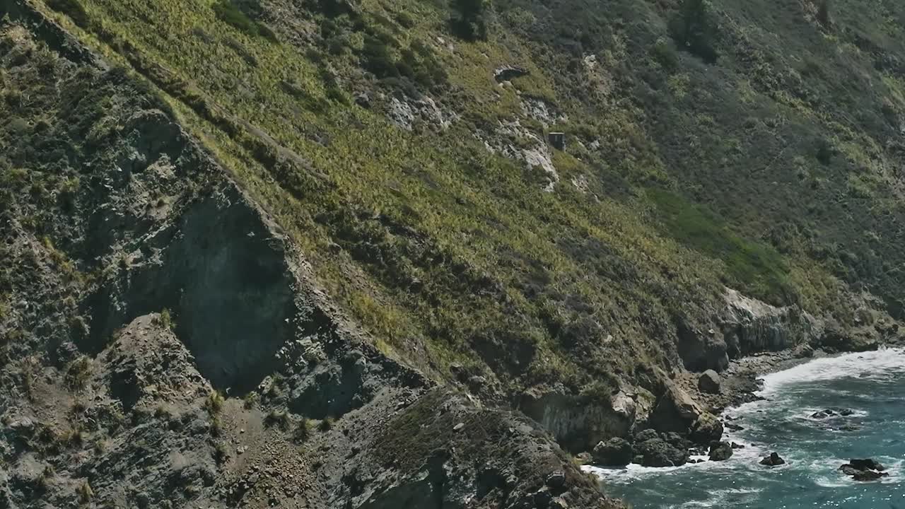Udsigt til klippekyst langs Californiens kystlinje med havbølger.