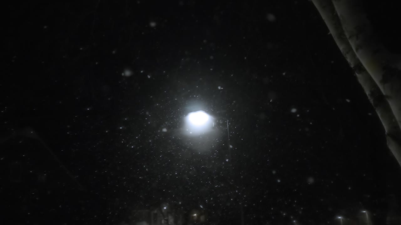 Looking up to dark sky in winter, snowfall in the lights of a street lamp, cold day with snowfall, static shot, background, slow motion snowflakes, copy space