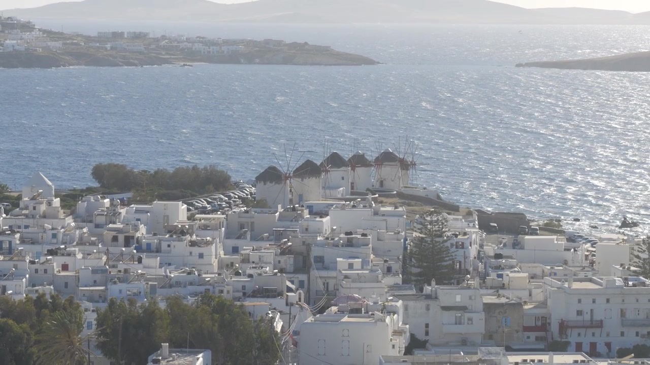 Mykonos, Grecia - Gli iconici mulini a vento imbiancati dominano un incantevole villaggio costiero, con acque blu scintillanti e uno scenario insulare mozzafiato - Ripresa panoramica verso l'alto.