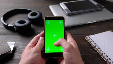 hands of man using smartphone with green screen on wood table