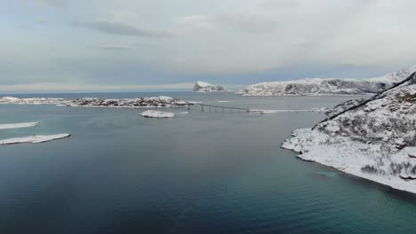 drone view in tromso area in winter flying over snowy islands with a bridge connecting white islands in norway