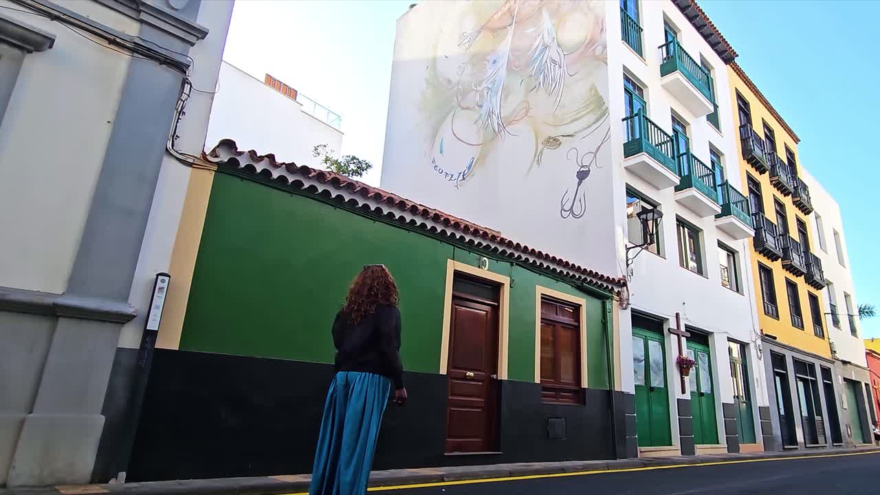 A person standing in front of a colorful mural on a street in Puerto, Spain