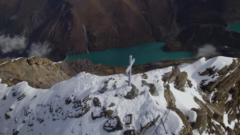 toma aérea de ojo de pájaro de la cruz en la cumbre con lago verde en el valle en invierno - zell am see, austria