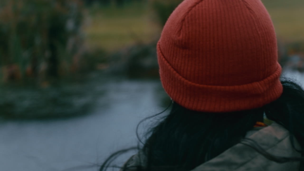 giovane donna solitaria che cammina nel parco indossando un berretto rosso godendosi la natura ragazza adolescente che si sente depressa durante una giornata nuvolosa con i capelli che soffiano dal vento