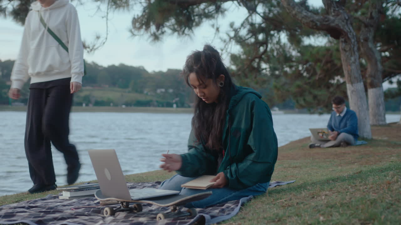 Ragazza asiatica che studia al parco con laptop e quaderno