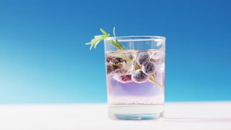 Close-up-of-transparent-drink-with-bluberries-on-blue-background