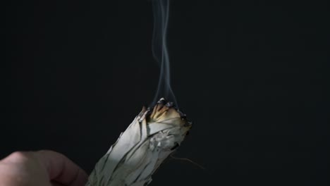 burning sage in a shell on a wood table with black background showing sage smoke