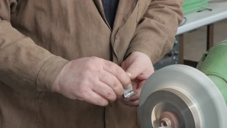 hands old master grind detail on bench grinder, rough grinding machine, close-up. work on pedestal grinder, items production. finish-grind metal part on factory