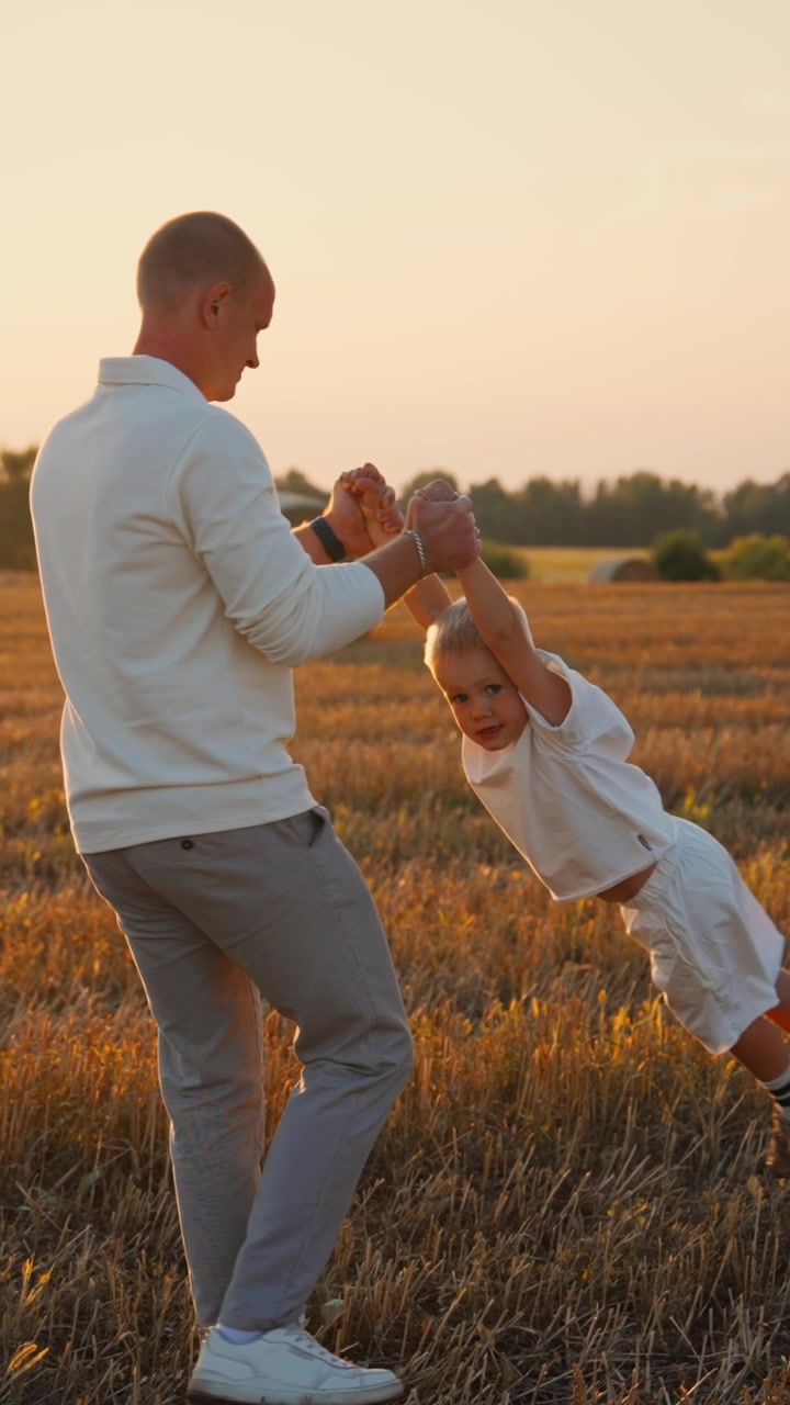 Padre che fa roteare il figlio piccolo in un campo di grano dorato al tramonto