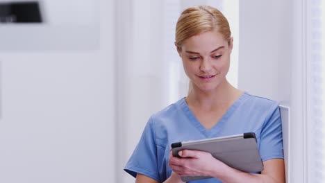 female doctor wearing scrubs in hospital corridor using digital tablet