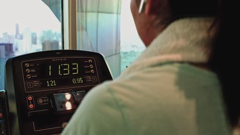 asian female exercising on treadmill at a gym with over the shoulder view of digital panel display.
