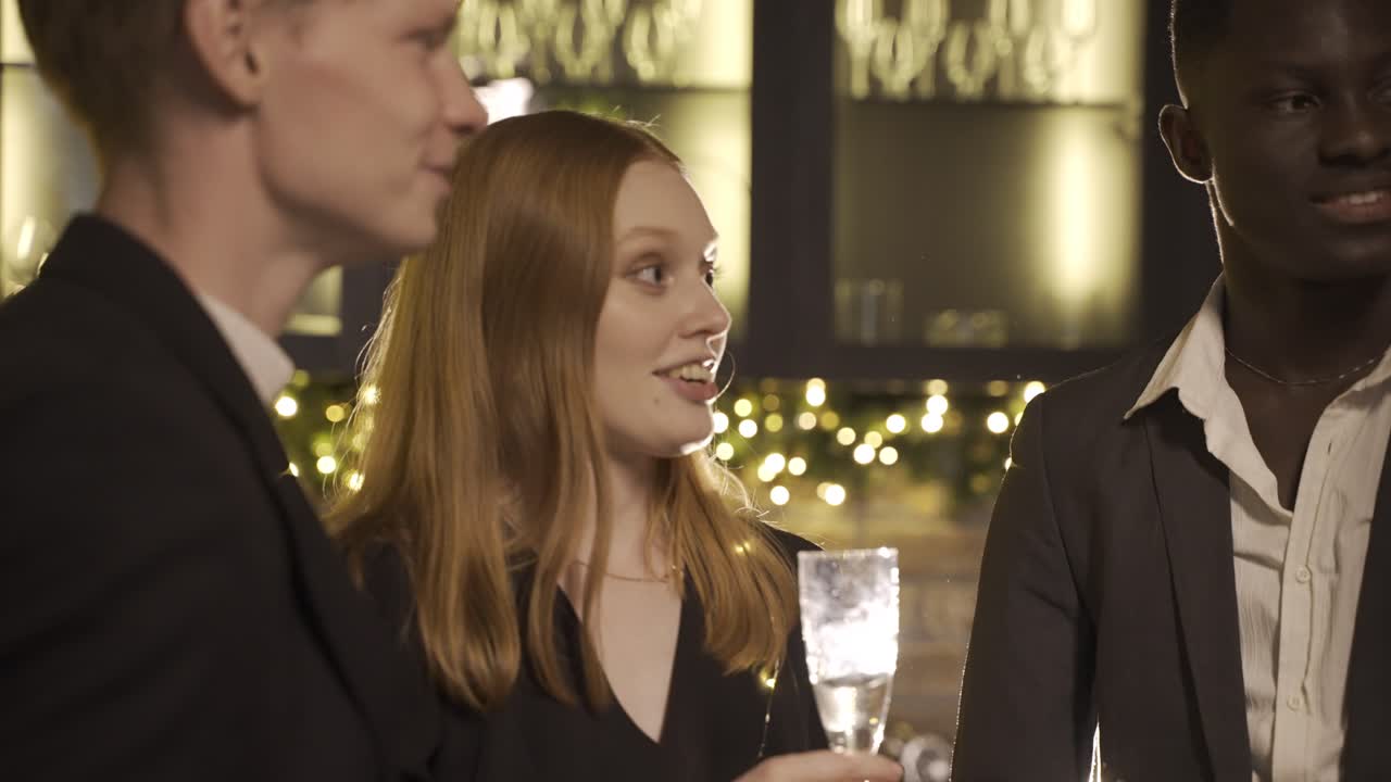 Close up view of group friends wearing stylish clothes while talking and holding champagne glasses at new year's party