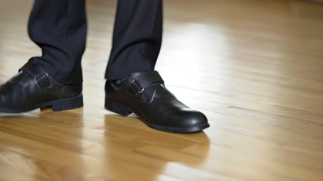 Man in black leather shoes dancing on the wooden floor. Male's legs in black trousers and new shoes shows some kind of dance on a parquet. Close-up