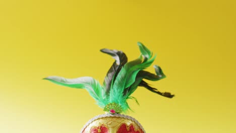 video of carnival masquerade mask with green feathers on yellow background with copy space