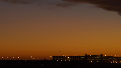 Toma-Panorámica-Derecha-Del-Aeropuerto-De-Barcelona-Iluminada-Al-Atardecer-Que-Revela-El-Aterrizaje-Del-Avión