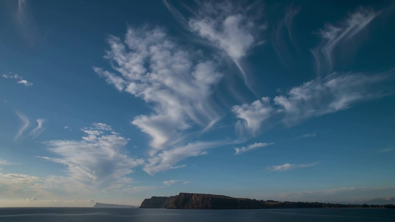Shifting cirrus clouds thickening, spreading over headland and sea, advecting with upper winds