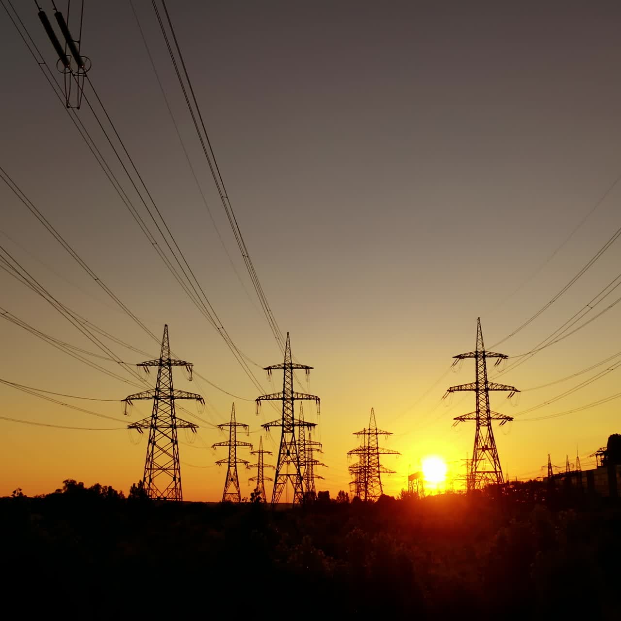Electric towers against the orange sunset. High voltage electric lines in the evening. Silhouettes of electrical pylons.