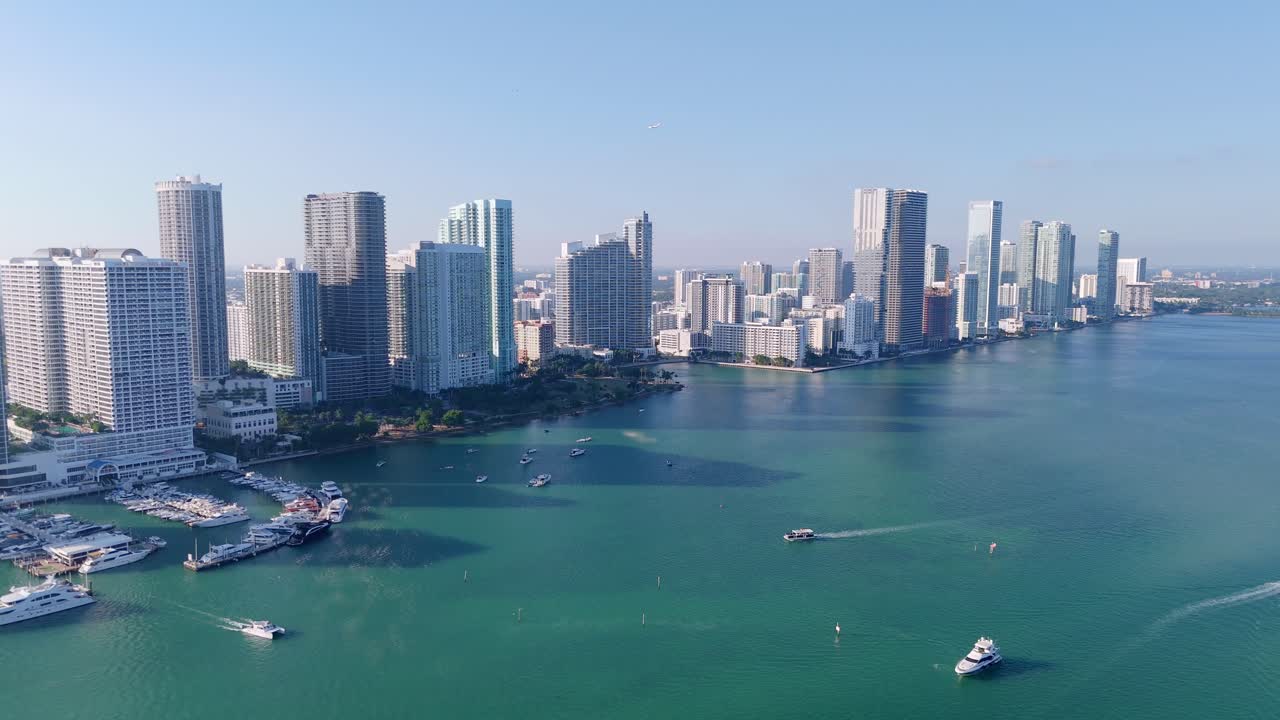Aerial drone view of downtown Miami’s waterfront skyline, featuring modern high-rise buildings, luxury yachts, and turquoise Biscayne Bay under a clear blue sky.