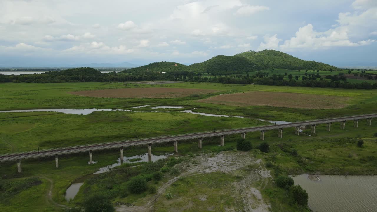 Aerial footage reversing away from a beautiful horizon with hills and a lake, farmland, elevated railway, manmade lake, in Saraburi, Thailand.