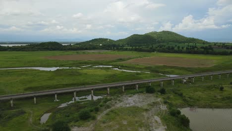 Aerial footage reversing away from a beautiful horizon with hills and a lake, farmland, elevated railway, manmade lake, in Saraburi, Thailand.