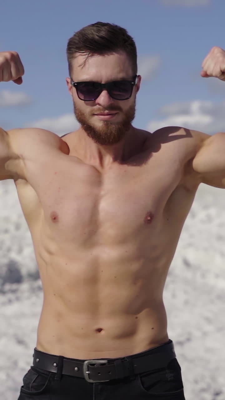 Athletic man shows his muscular body outdoors. Portrait of a shirtless sportsman with trained body on white canyon background in sunny daytime. Vertical video