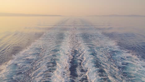 Slow-motion-view-of-the-wake-water-trace-behind-a-ferry-at-sea-at-sunrise,-sunset