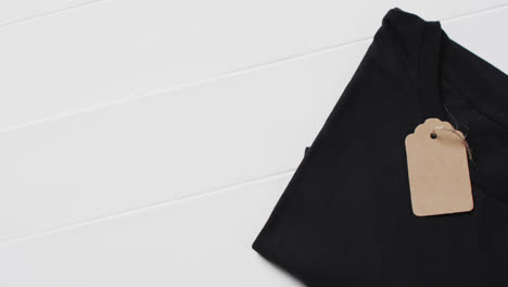 Video-of-flat-lay-of-black-t-shirt-with-tag-and-copy-space-on-white-background