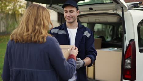 Frau-Trifft-Einen-Gutaussehenden,-Freundlichen-Liefermann-Und-Nimmt-Einen-Paketkasten-Neben-Dem-Lieferwagen.-Kurier-Macht-Sich-Notizen-Zum-Paket