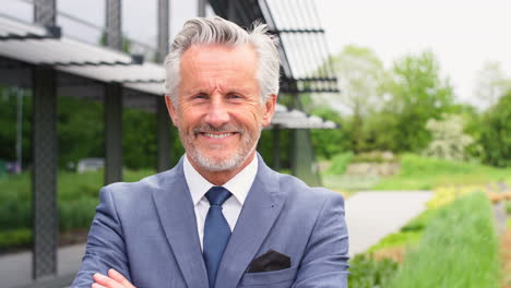 portrait of smiling senior businessman ceo chairman standing outside modern office building