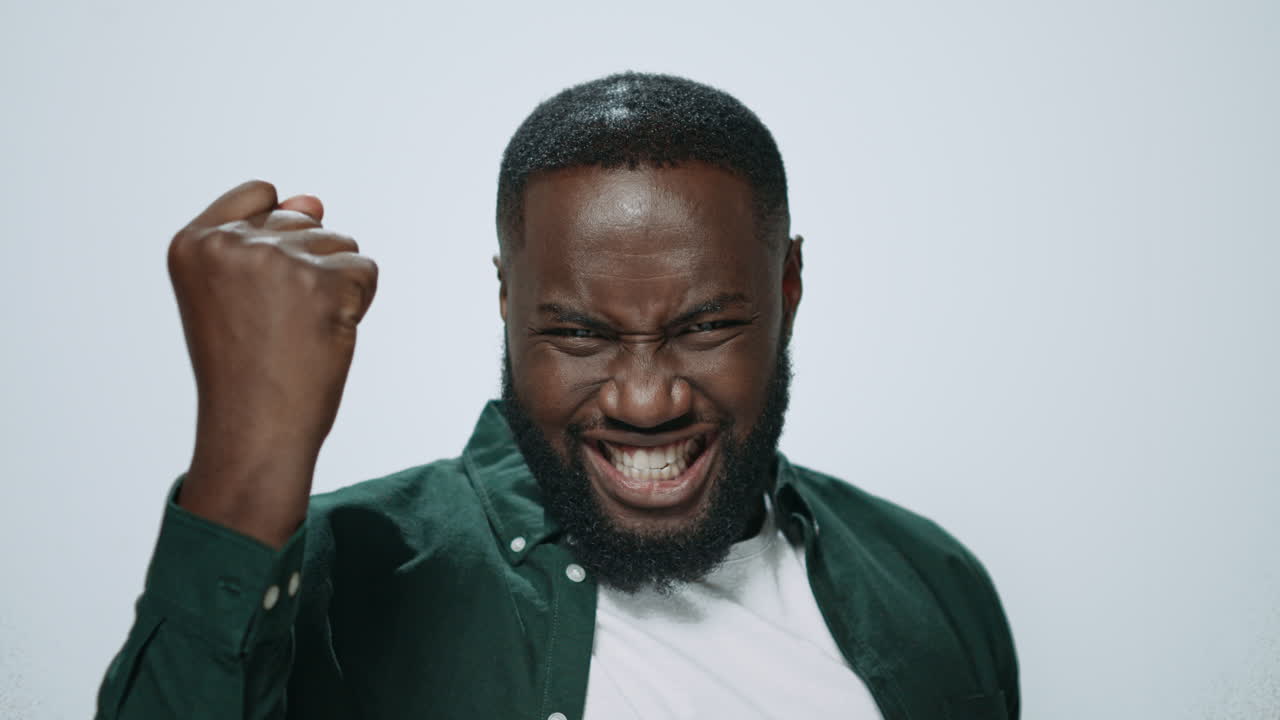 Ritratto di uomo africano sorridente che fa il gesto del sì su sfondo grigio.