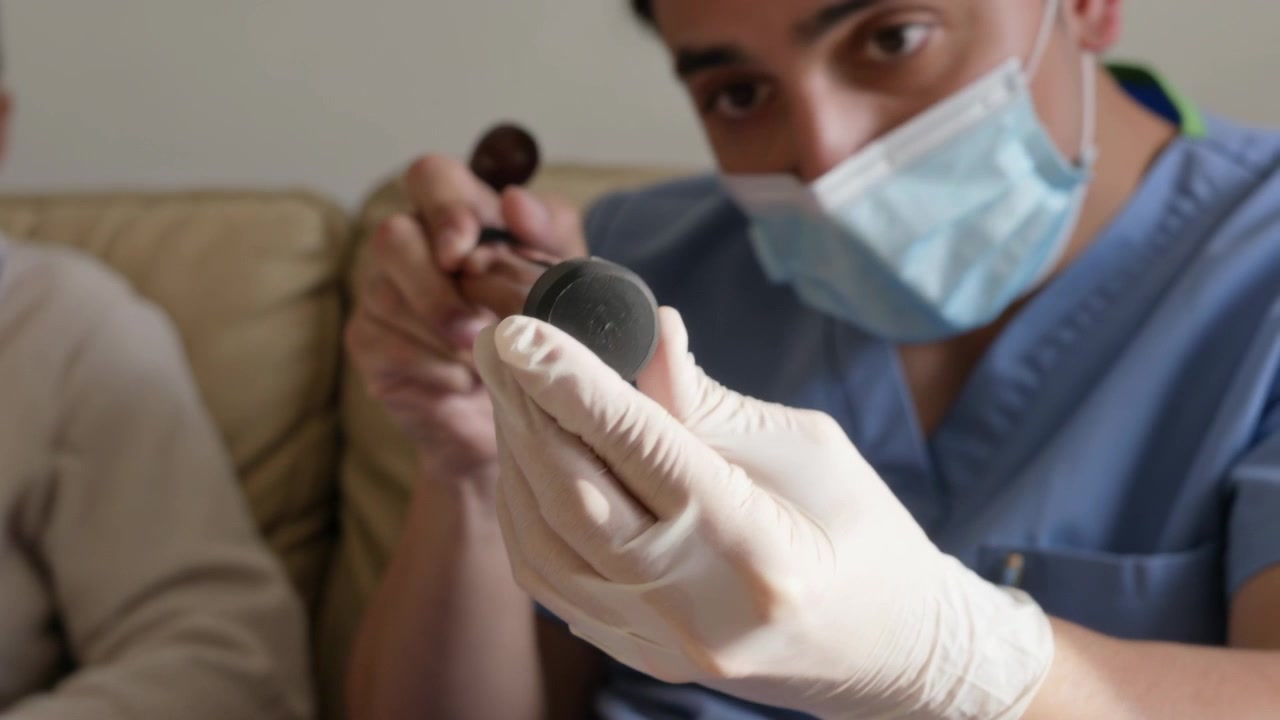 Cuidador usando luvas e uniforme cirúrgico, girando a ponteira de borracha de uma bengala em casa, verificando o desgaste.