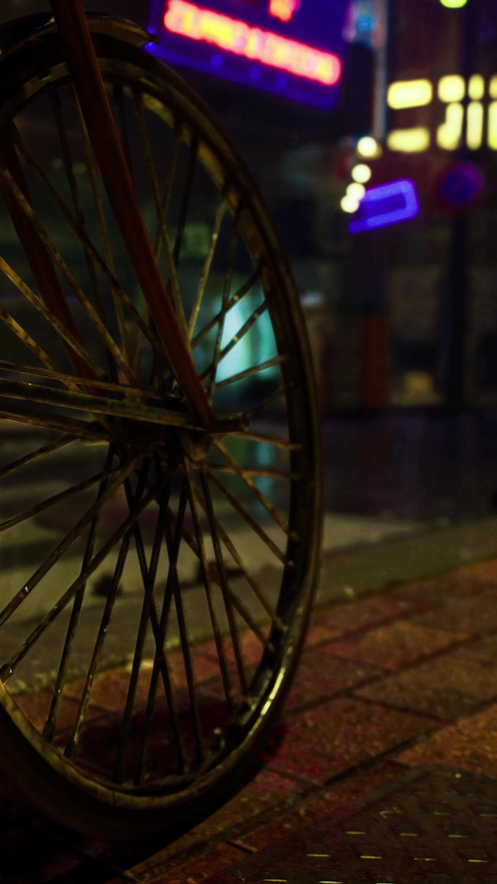 Ruota di bicicletta su strada bagnata con luci colorate in un contesto urbano di notte
