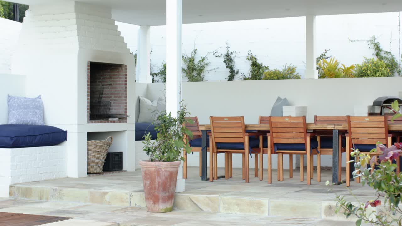 La telecamera sta panoramando a destra attraverso il patio per mostrare un barbecue, una panca imbottita e un tavolo da pranzo.