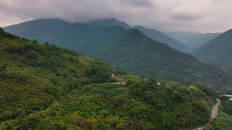 Ascending-drone-shot-of-green-growing-mountains-with-traffic-on-road-during-grey-day-in-Taiwan-in-Wulai-District-烏來-區-in-Taiwan