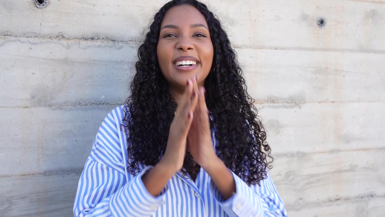 A confident young woman is smiling brightly while standing against a concrete wall backdrop