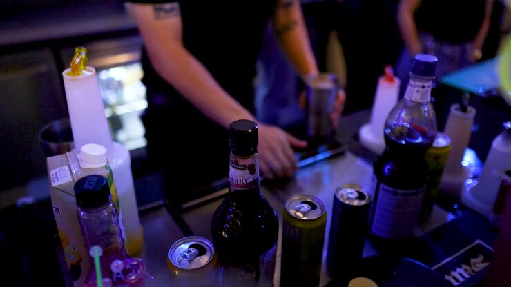 Un barista prepara cocktail con un misurino per il ghiaccio sotto luci colorate in un vivace bar notturno di Bangkok