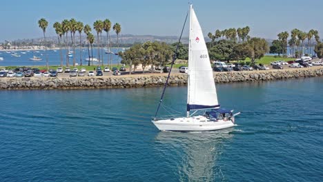 Panning-Drone-shot-of-Sail-Boat-heading-out-of-San-Diego-bay-over-to-Sail-boats-ancored-in-the-harbor-in-California