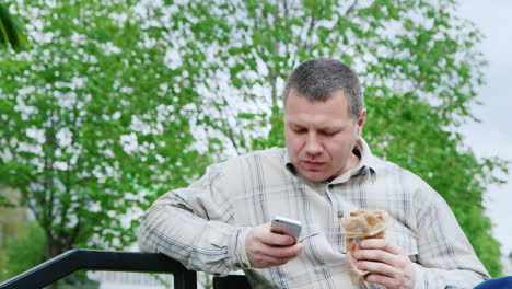 Der-Mann-Im-Park,-Der-Fast-Food-Isst,-Benutzt-Dein-Smartphone