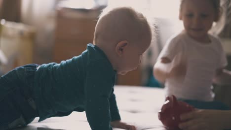 cute baby crawls to elder sister kicking piggybank on bed