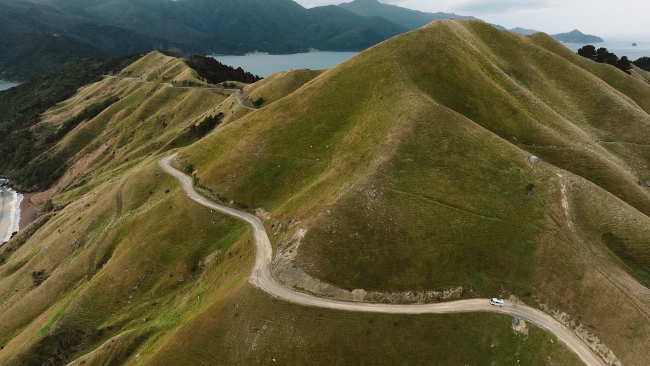 Aerial of tourist campervan driving on idyllic winding mountainous road with ocean views through Te Aumiti French Pass in Marlborough Sounds, South Island of New Zealand Aotearoa