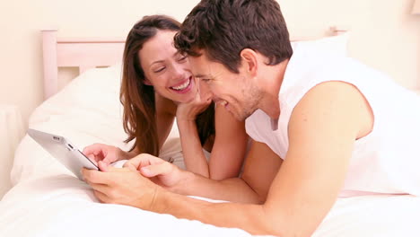 una pareja feliz acostada en la cama usando una tableta