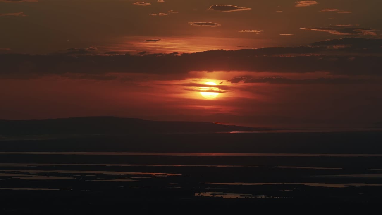 Drone view from Bountiful Canyon in Utah of a golden summer sunset over Salt Lake Valley with clouds, mountains, and water ponds reflecting light from the Great Salt Lake