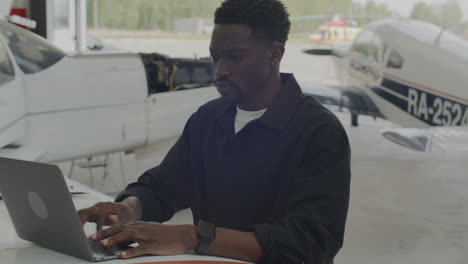 technician typing aircraft data on laptop in maintenance hangar