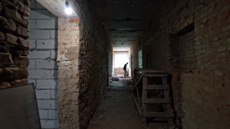 moving by the long corridor of an old building of red bricks. approaching a builder laying bricks at the end of the hall.